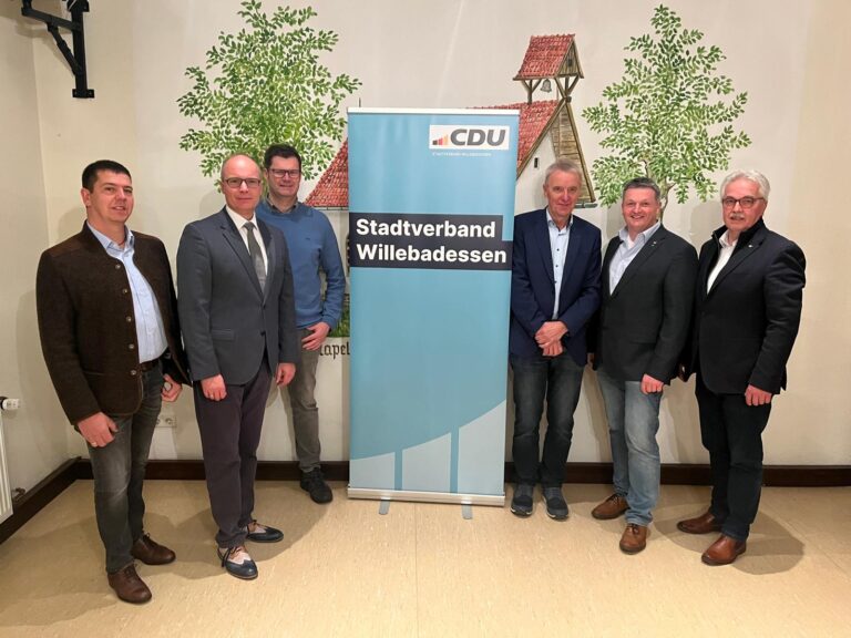 Sechs Männer stehen um ein CDU-Banner vor einer Wand mit einem Bild einer Kapelle