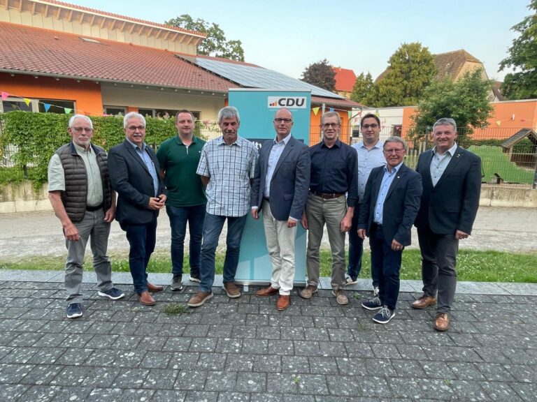 9 Männer stehen an einem Sommerabend draußen vor einem hellblauen Werbeaufsteller der CDU