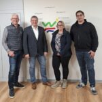 Drei Männer und eine Frau stehen vor einer weißen Wand in einem Raum. Auf der Wand ist das Logo der Stadt Willebadessen und die Namen der Ortsteile.